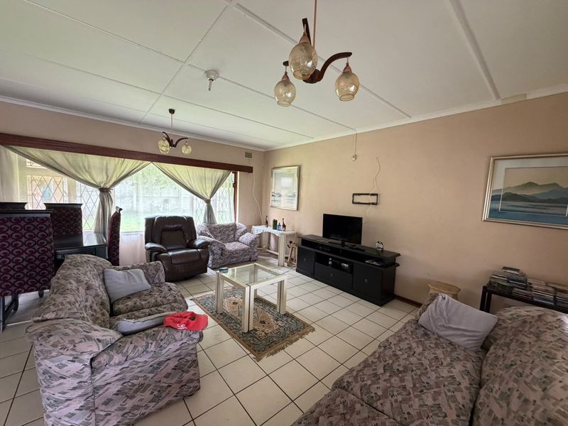 Spacious living room featuring tiled flooring and large windows with security bars, requiring cosmetic updates to the ceiling and wall finishes.
