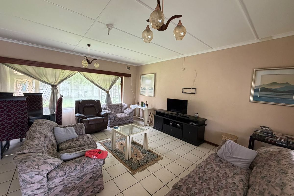 Spacious living room featuring tiled flooring and large windows with security bars, requiring cosmetic updates to the ceiling and wall finishes.