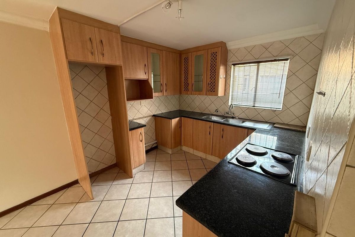 A functional kitchen featuring laminate cabinetry, granite countertops, an electric hob, and tiled finishes throughout.