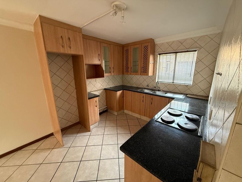 A functional kitchen featuring laminate cabinetry, granite countertops, an electric hob, and tiled finishes throughout.