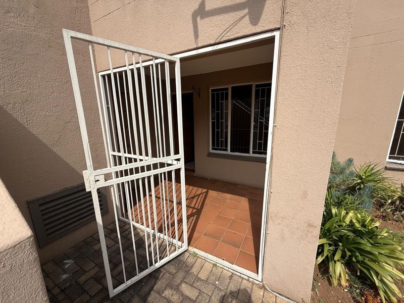 A covered patio area featuring tiled flooring, a security gate, and window security bars, providing a functional outdoor entrance space.