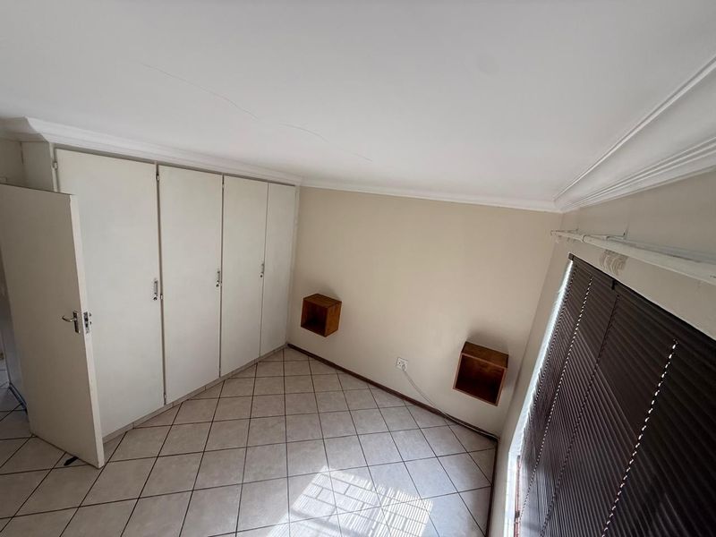 A vacant bedroom featuring tiled flooring, built-in cupboards, and venetian blinds, offering a clean and functional space ready for personalization.