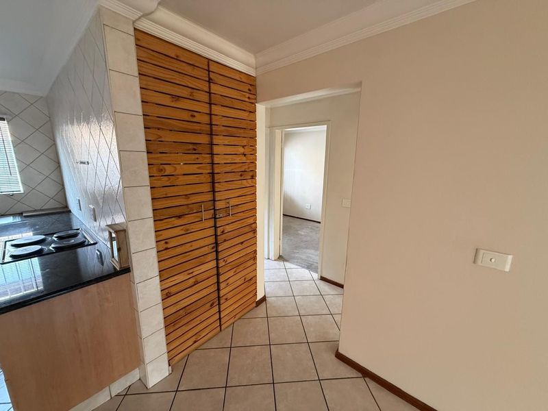 A functional kitchen area featuring tiled flooring, black granite countertops, an electric hob, and built-in wooden cabinetry, leading into a hallway.