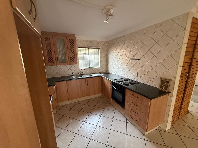 A functional kitchen featuring laminate cabinetry, granite countertops, a built-in oven with electric hob, and tiled flooring.