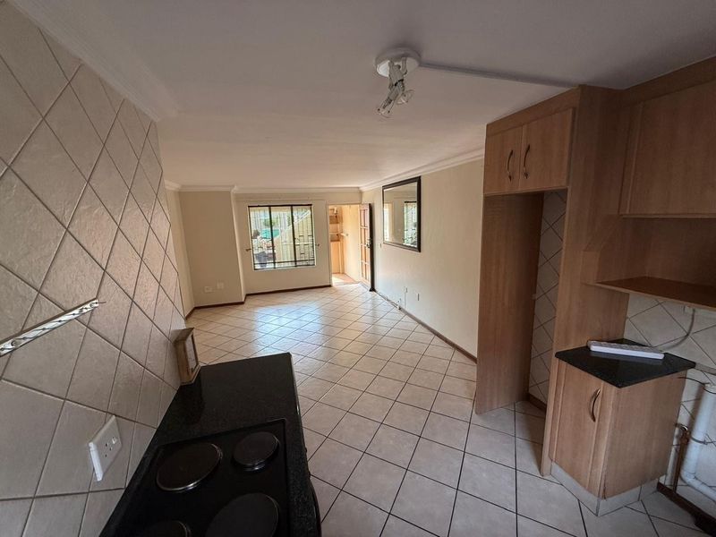 Open-plan living area featuring tiled flooring, built-in kitchen cabinetry with granite countertops, and an electric hob, leading to an exterior entrance.