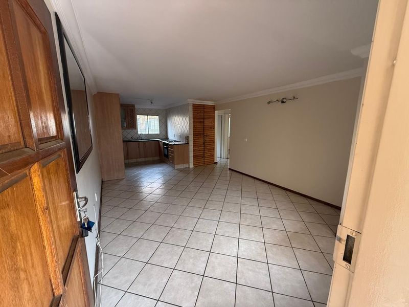 An open-plan living and kitchen area featuring tiled flooring, built-in cabinetry, and integrated cooking appliances in a neutral, well-maintained space.