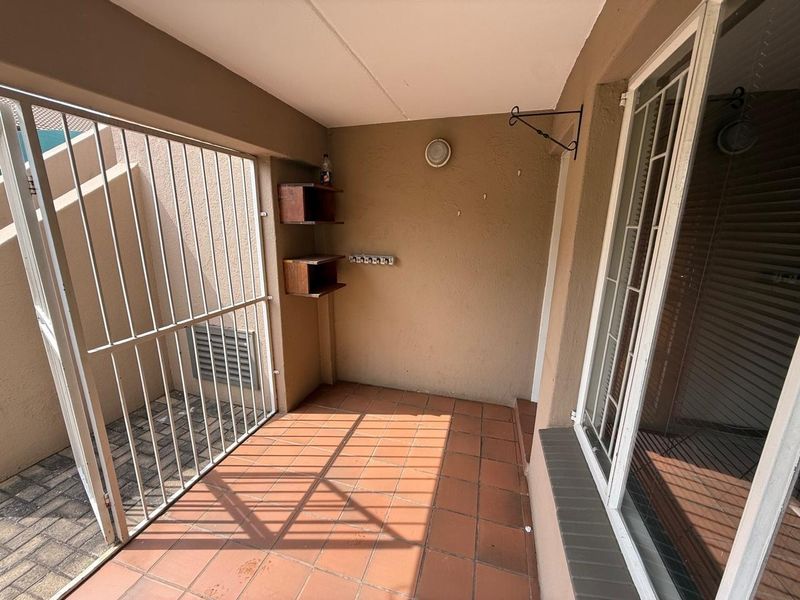 A covered patio area featuring tiled flooring, a security gate, and wall-mounted shelving, providing a functional outdoor space.