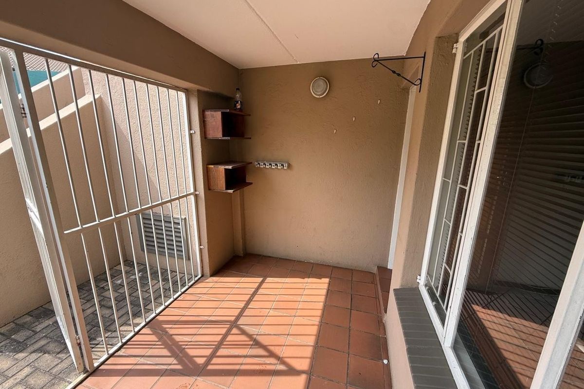 A covered patio area featuring tiled flooring, a security gate, and wall-mounted shelving, providing a functional outdoor space.