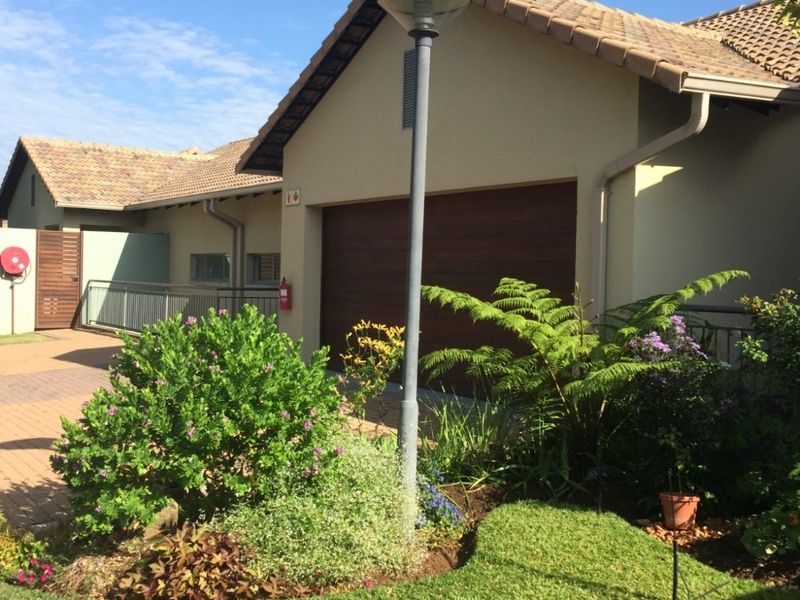 Front exterior view of a retirement village unit featuring a tiled roof, garage, and well-maintained landscaped garden area.
