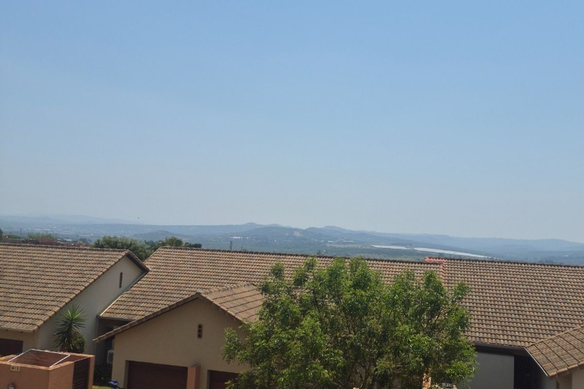 An elevated view of a residential retirement village featuring tiled roof homes, double garages, and paved driveways with distant landscape views.