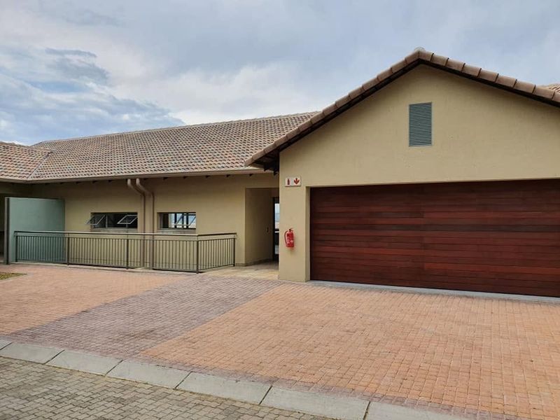 Front elevation of a retirement village unit featuring a paved driveway, timber garage door, and metal balustrade detailing.