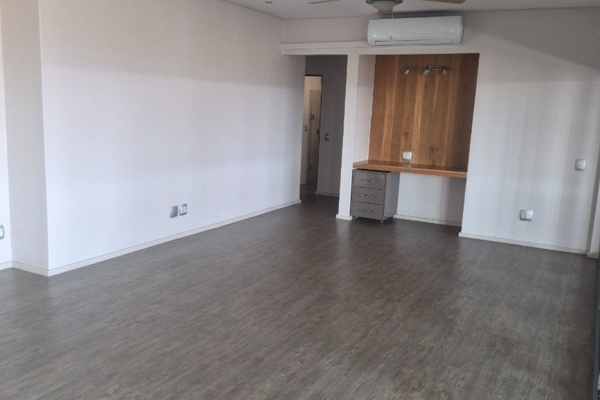 Spacious open-plan living area featuring modern laminate flooring, a built-in desk nook, ceiling fan, and split-system air conditioning.