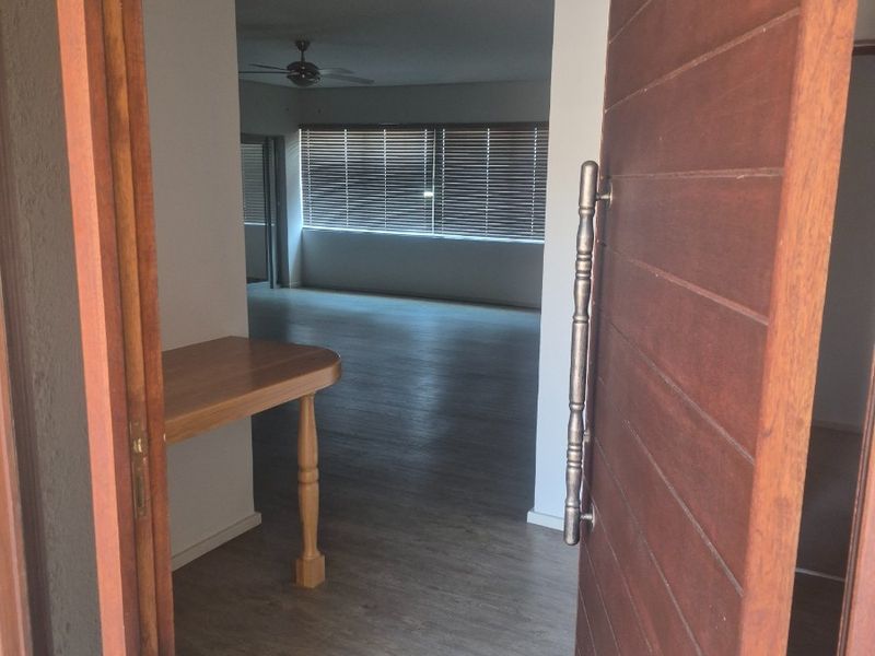 An inviting entrance area featuring a solid timber front door, leading into an open-plan living space with laminate flooring and neutral finishes.