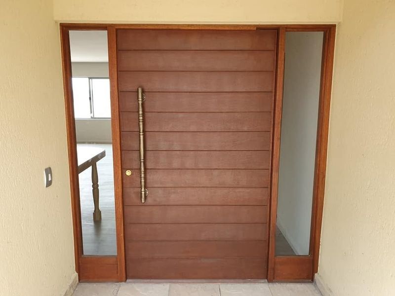 A well-maintained solid timber front door featuring vertical handle hardware and flanking sidelight windows, providing a secure and welcoming entrance to the residence.