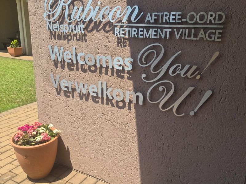 Entrance area of Rubicon Retirement Village featuring a textured masonry wall with prominent metal signage and paved walkway.