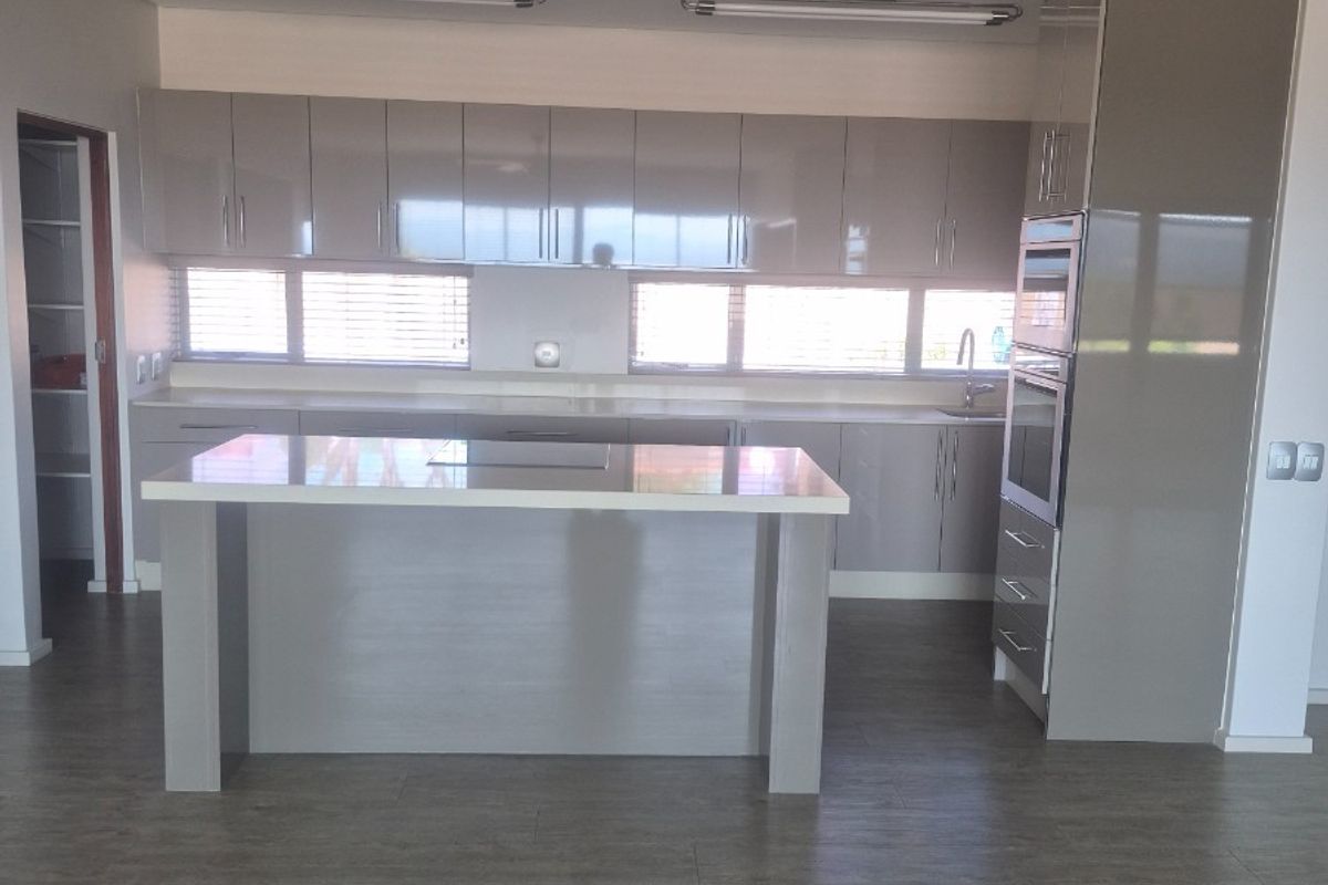 Modern kitchen featuring glossy cabinetry, a central island, built-in appliances, and stone benchtops, offering a clean and functional space.