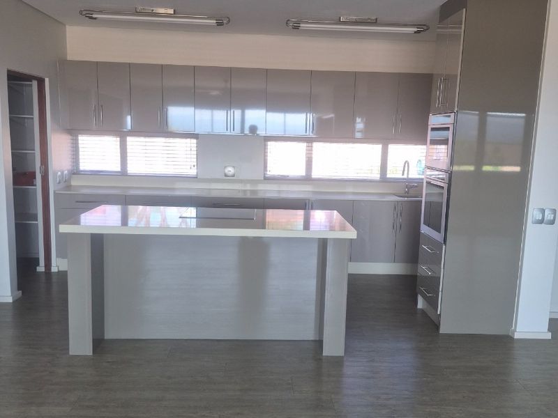 Modern kitchen featuring glossy cabinetry, a central island, built-in appliances, and stone benchtops, offering a clean and functional space.