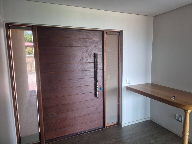 A modern entrance featuring a large timber pivot door with sidelight windows and a built-in wooden console shelf.
