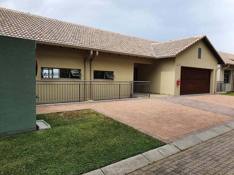 Front elevation of a retirement village unit featuring a paved driveway, sectional garage door, and metal safety railings.