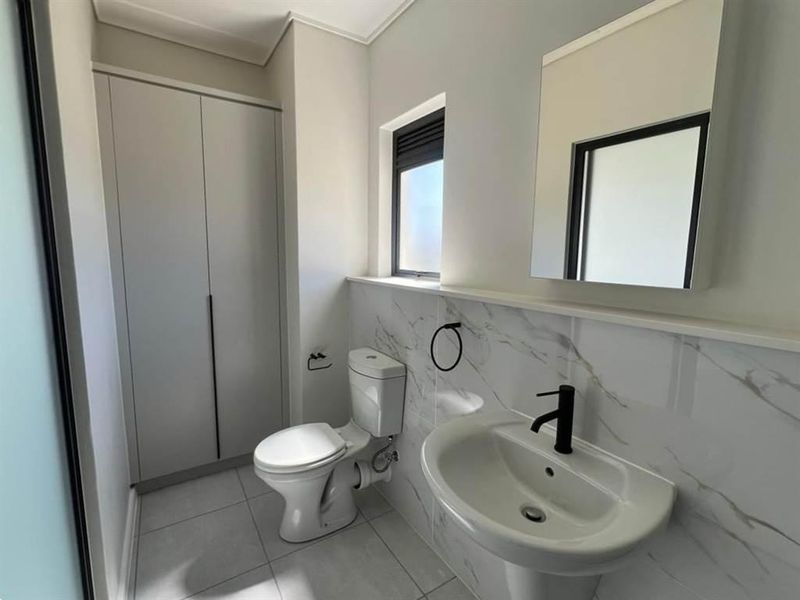 A modern, clean bathroom featuring a pedestal basin, toilet, built-in storage cupboard, and elegant marble-look wall tiling.