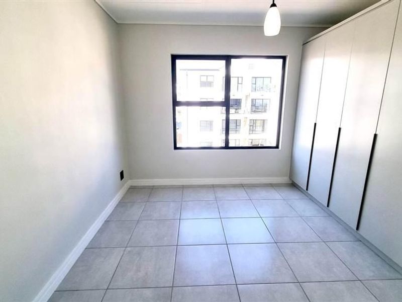 A bright, empty bedroom featuring neutral tiled flooring, built-in cupboards, and a large window providing natural light.