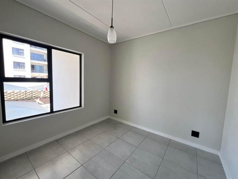 A clean, empty bedroom featuring neutral grey walls, large aluminium-framed windows, and modern tiled flooring, ready for personalization.