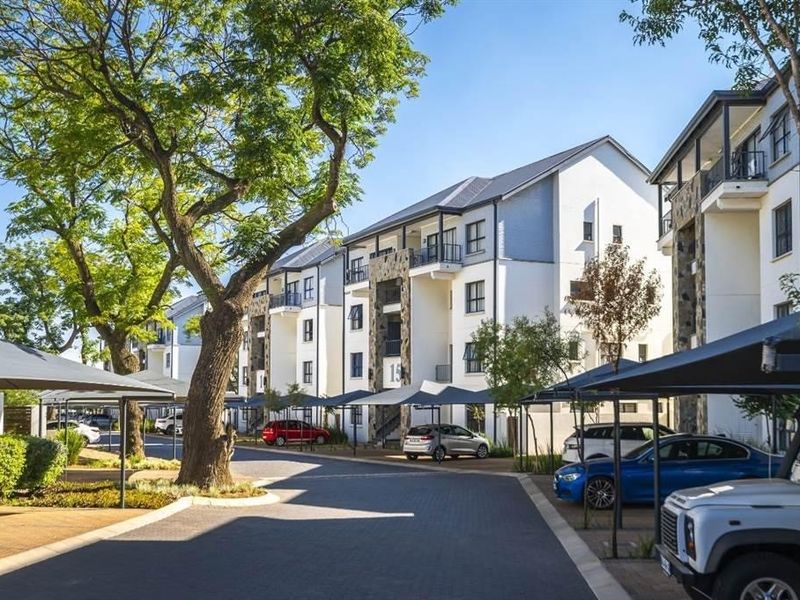 A well-maintained apartment complex exterior featuring paved driveways, covered parking bays, and modern building facades with stone cladding accents.