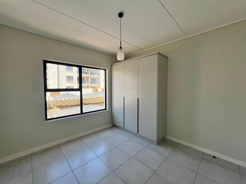 A clean, modern bedroom featuring neutral tiled flooring, a built-in wardrobe, and a large window providing natural light.