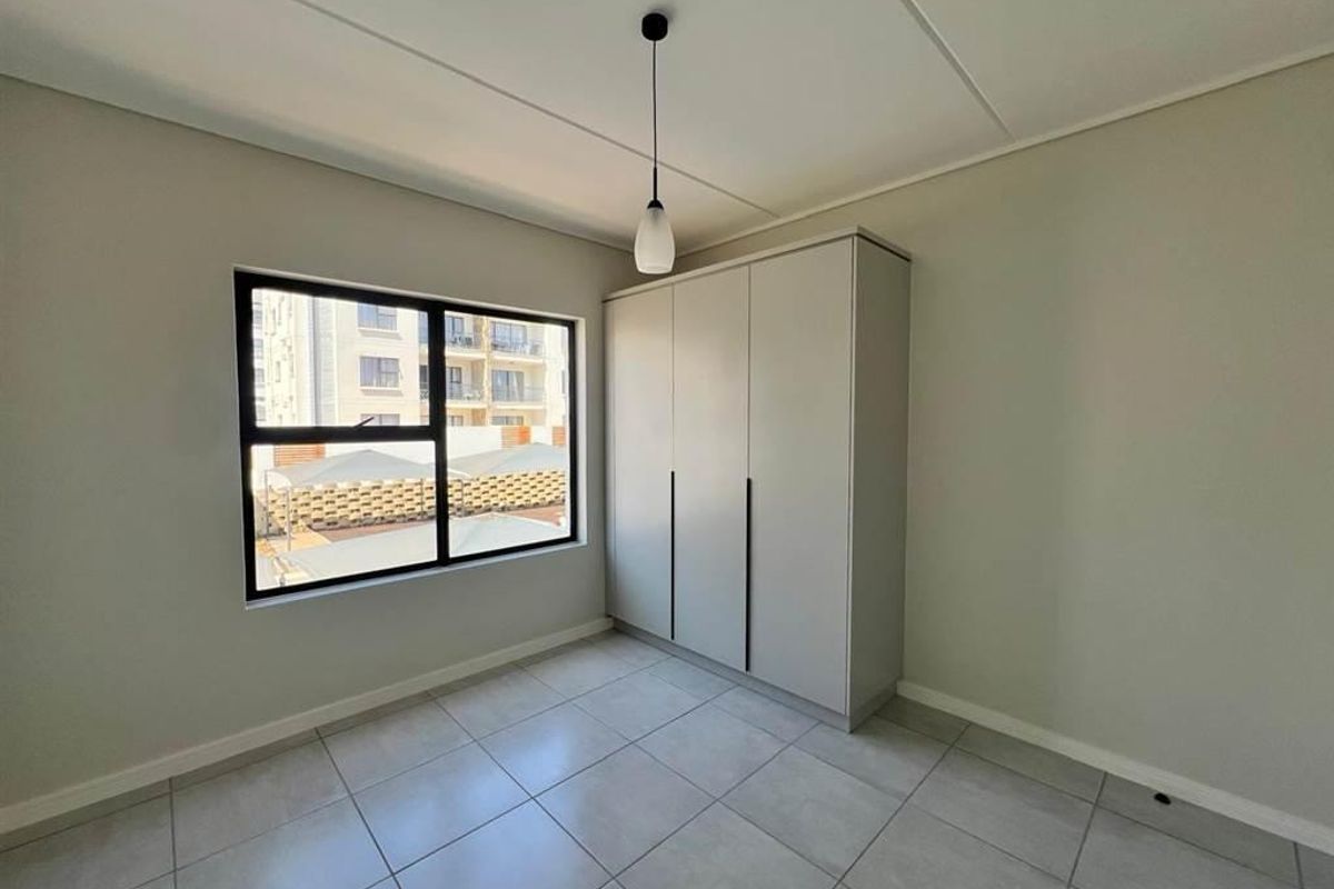 A clean, modern bedroom featuring neutral tiled flooring, a built-in wardrobe, and a large window providing natural light.