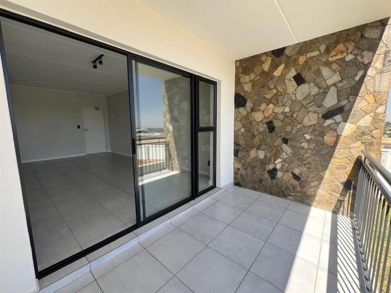 A spacious balcony featuring modern tiled flooring, a decorative stone feature wall, and a metal balustrade, offering seamless access to the interior living area.