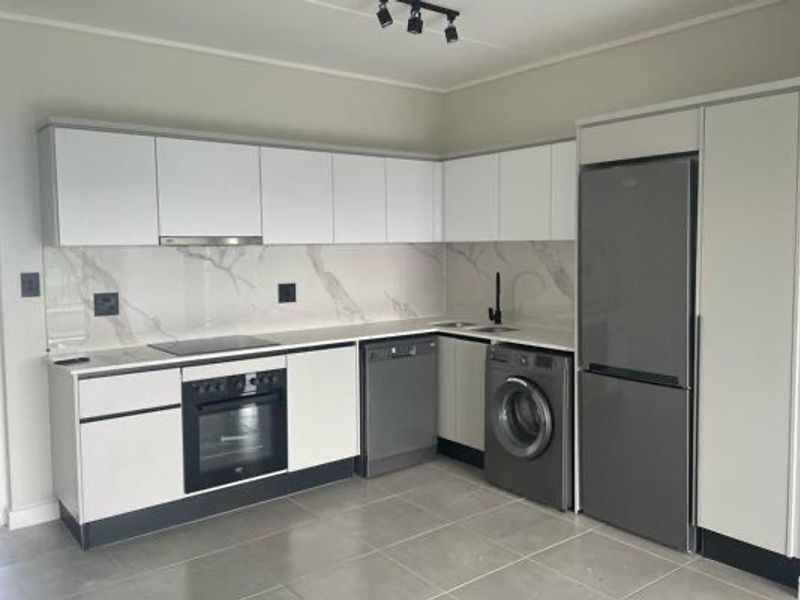 Modern kitchen featuring sleek white cabinetry, stone-look splashback, integrated appliances, and contemporary track lighting in a clean, minimalist space.