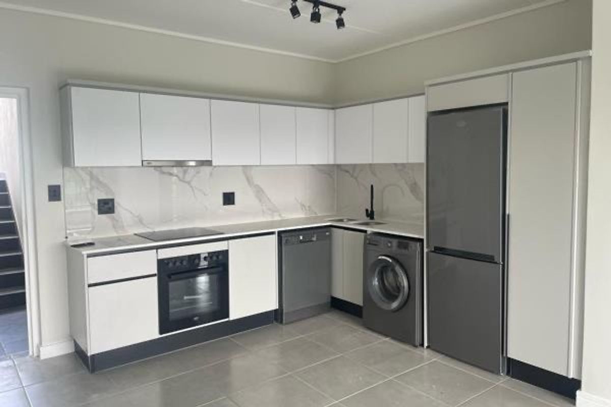 Modern kitchen featuring sleek white cabinetry, stone-look splashback, integrated appliances, and contemporary track lighting in a clean, minimalist space.