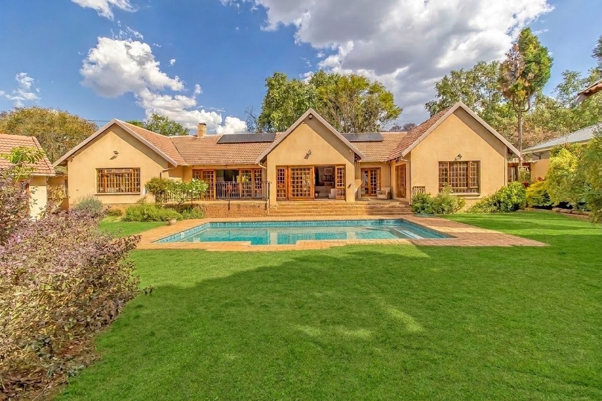 Rear view of the property featuring a well-maintained swimming pool, brick patio, landscaped garden, and a tiled roof with integrated solar panels.