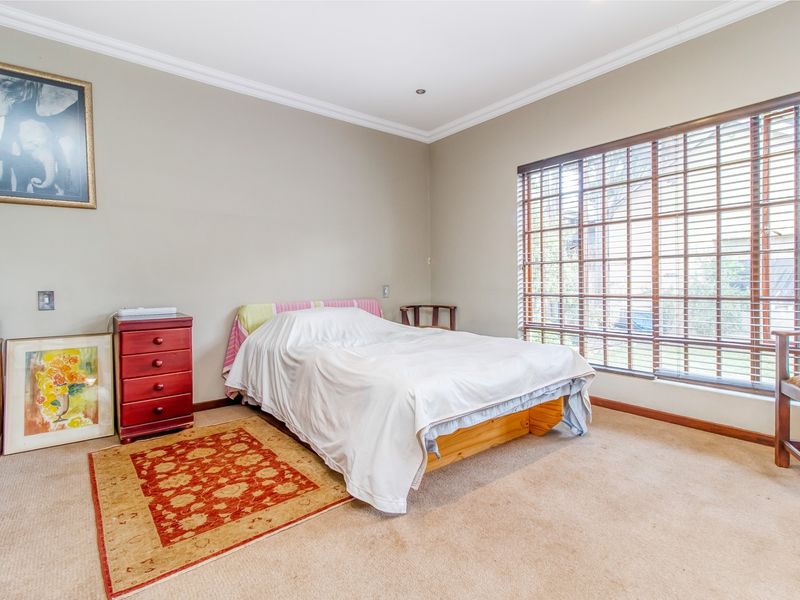 A well-lit bedroom featuring neutral wall tones, carpeted flooring, and a large window fitted with venetian blinds.