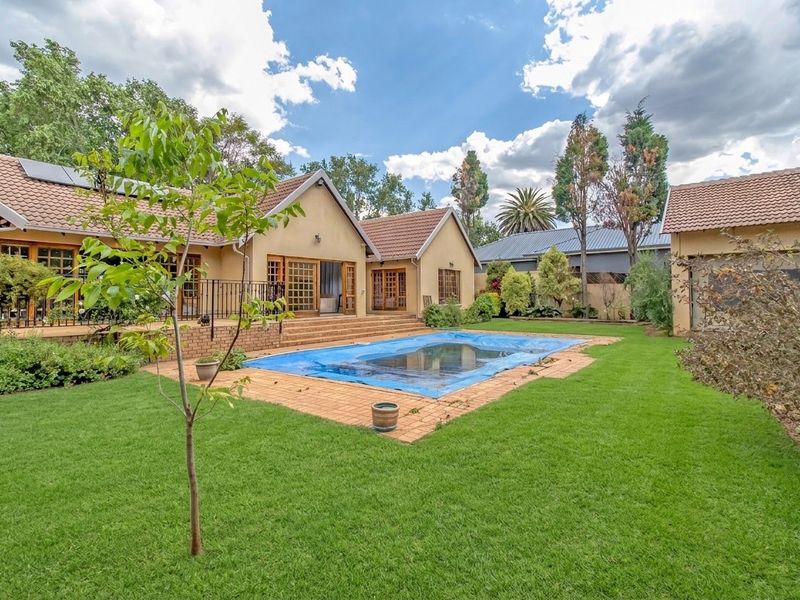Spacious rear garden featuring a swimming pool with cover, brick patio area, and well-maintained lawn, set against the rear elevation of the house.