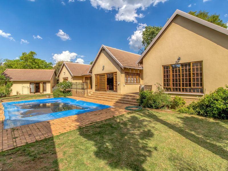 Rear view of the property featuring a swimming pool with cover, paved patio area, and well-maintained garden with established landscaping.