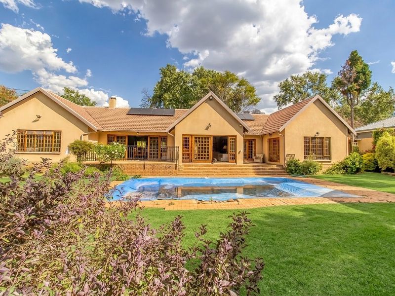 Spacious rear exterior view featuring a well-maintained garden, swimming pool with cover, and a large patio area leading into the home.