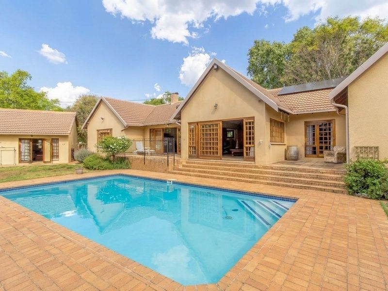 A spacious rear garden featuring a swimming pool, brick-paved patio area, and direct access to the home through multiple timber-framed glass doors.