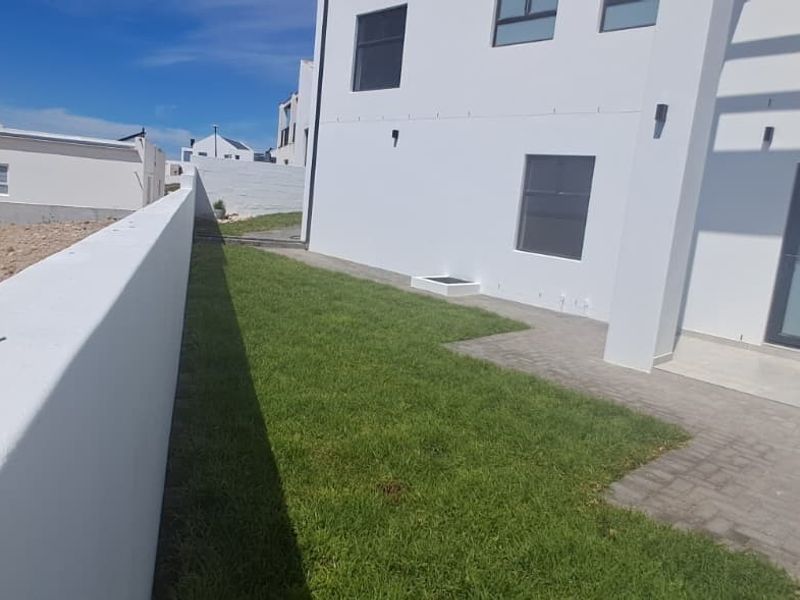Rear exterior view showing a paved patio area, a small lawn, and a high boundary wall against a modern white building facade.