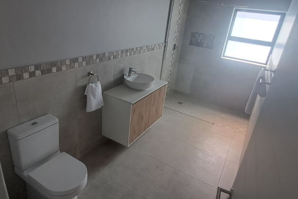 A modern, well-maintained bathroom featuring a wall-mounted vanity with a vessel sink, a walk-in shower, and neutral floor-to-ceiling tiling.