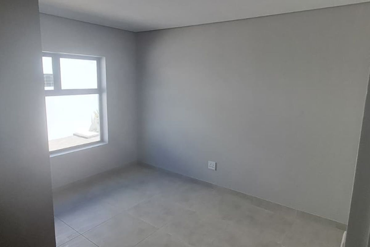 A clean, empty bedroom featuring neutral grey tiled flooring, smooth walls, and a modern aluminium window frame, offering a blank canvas for interior design.