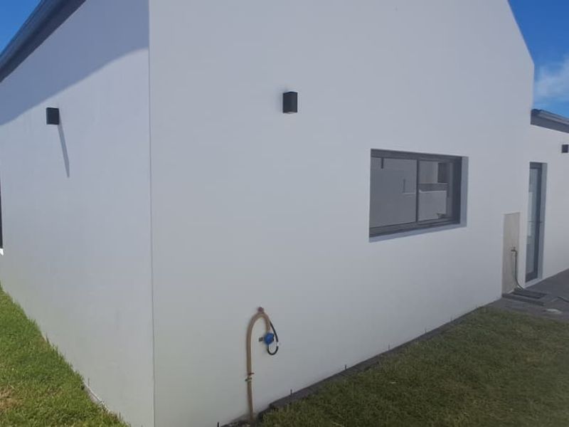 A well-maintained rear exterior view of the property featuring clean white rendered walls, modern aluminium window frames, and a neat lawn area.