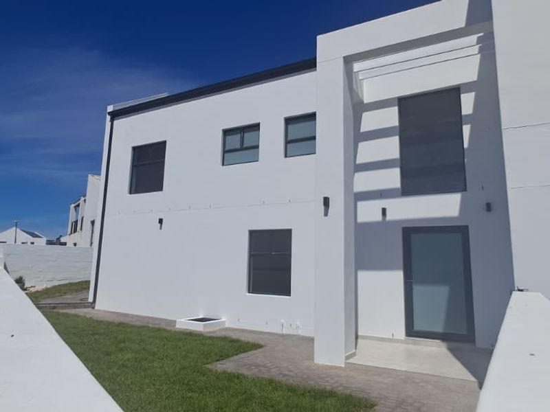 Modern double-story residential facade featuring clean white lines, paved entrance walkway, manicured lawn, and integrated garage access.