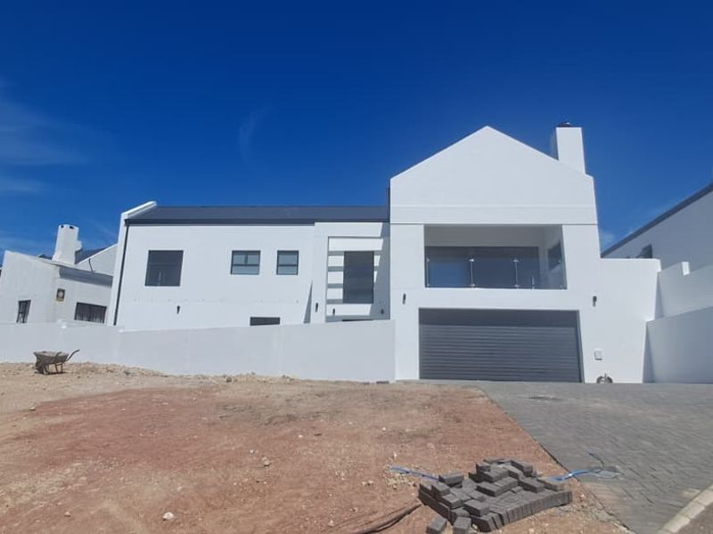 Modern white multi-level residential facade featuring a garage, paved driveway, and upper-level balcony with glass balustrade, set against a clear blue sky.