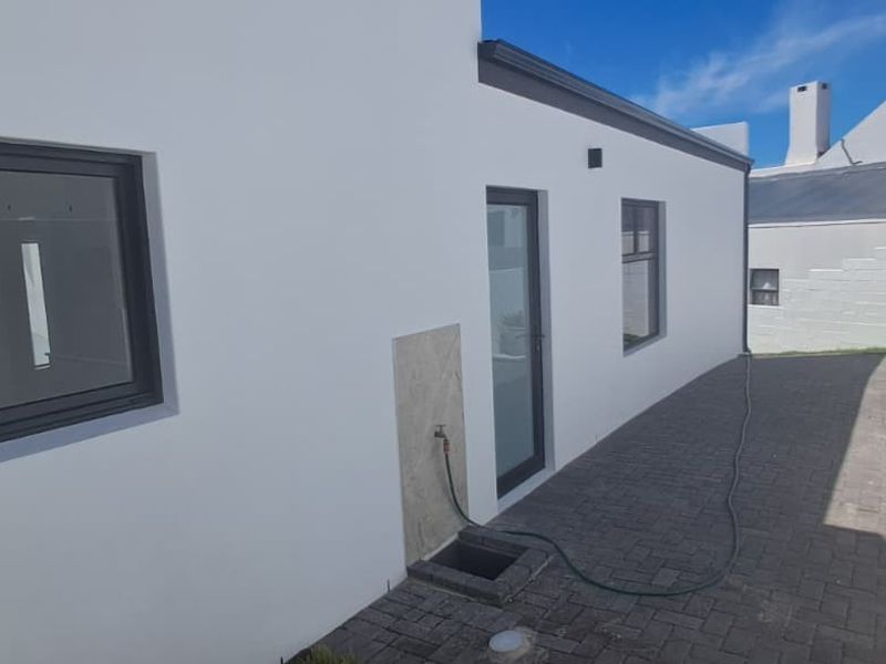 A clean rear exterior view featuring a paved walkway, modern white rendered walls, and dark aluminium window and door frames.