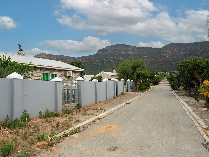 A street-level view of the property featuring a solid boundary wall, metal gate, and mountain backdrop in a quiet residential setting.
