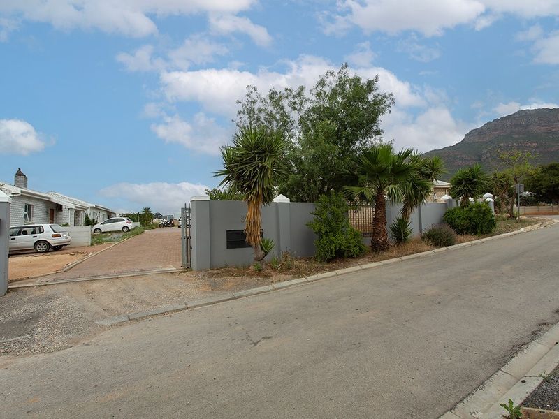 Street view of the property entrance featuring a paved driveway, secure boundary wall, and established landscaping with mountain views in the background.