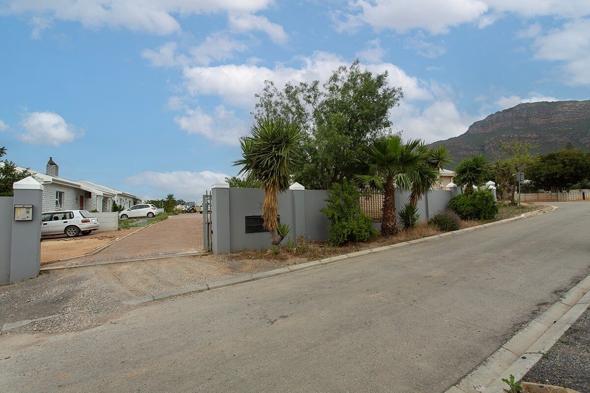 Street view of the property entrance featuring a paved driveway, secure boundary wall, and established landscaping with mountain views in the background.