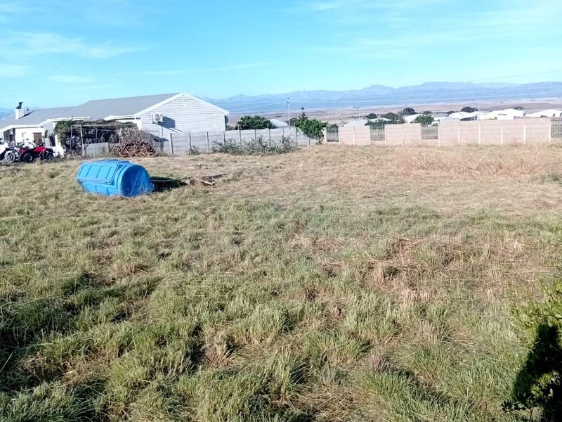 An expansive, undeveloped plot of land featuring natural grass coverage and enclosed by a precast concrete boundary wall with distant mountain views.