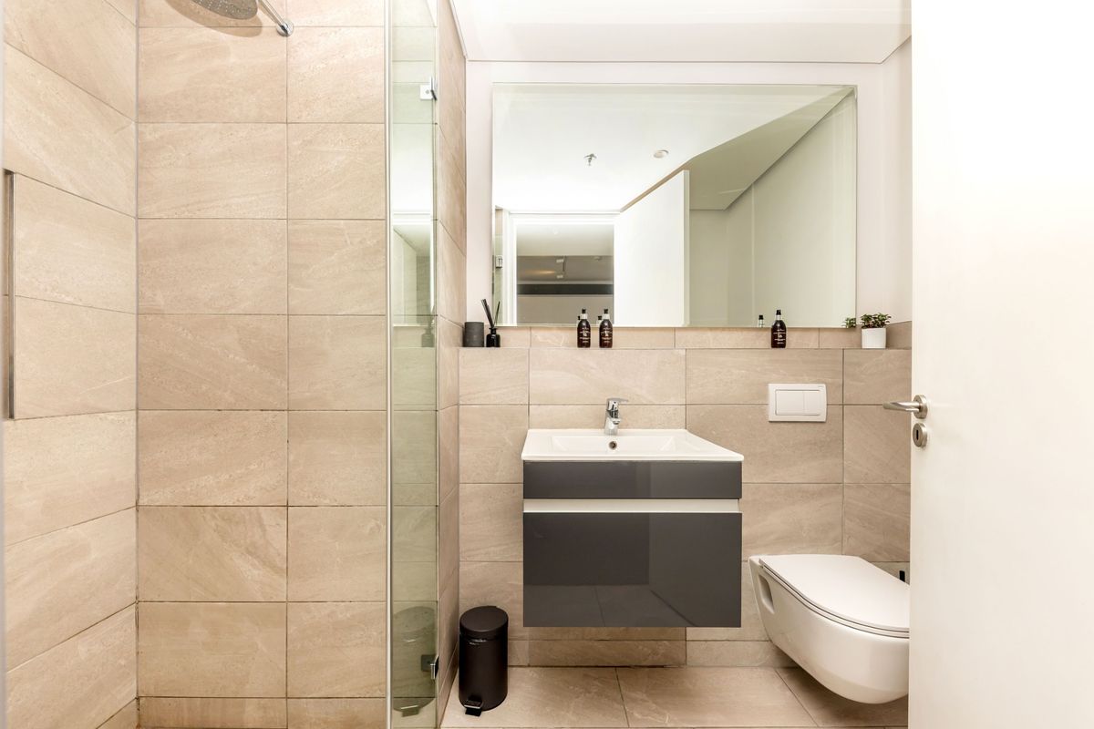 Modern bathroom featuring a wall-mounted vanity, wall-hung toilet, and a spacious walk-in shower with neutral floor-to-ceiling tiling.